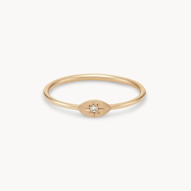 The visionary evil eye ring by bluboho is a thin, 14k yellow gold ring featuring a brilliant diamond set in an oval-shaped, starburst design on a plain background.