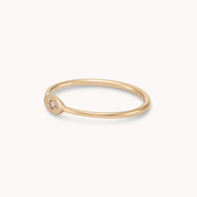 The bluboho "Visionary Evil Eye Ring" in 14k yellow gold, showcasing a thin band and a small, flat oval centerpiece with a tiny embedded diamond at the center, is displayed against a plain white background.